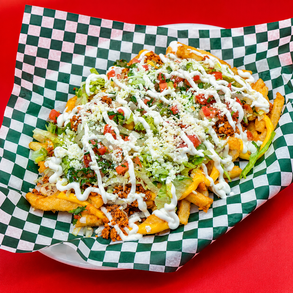Loaded fries topped with lettuce, tomatoes, seasoned meat, cheese, and creamy white sauce in a checkered paper-lined basket.