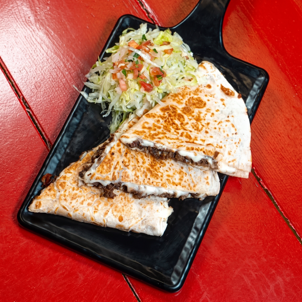 Grilled cheese-filled quesadilla wedges with beef, shredded lettuce, pico de gallo, and sour cream on a black plate.